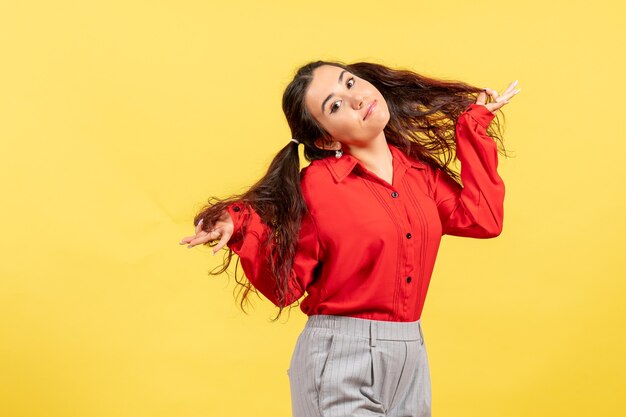 Chica joven en blusa roja posando de manera coqueta en amarillo