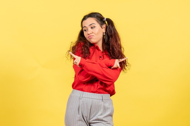 Chica joven en blusa roja señalando con el dedo sobre amarillo