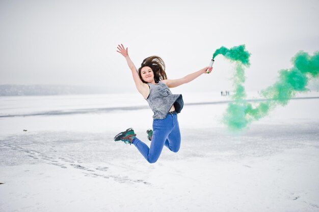 Chica joven con bomba de humo de color verde en la mano en el día de invierno