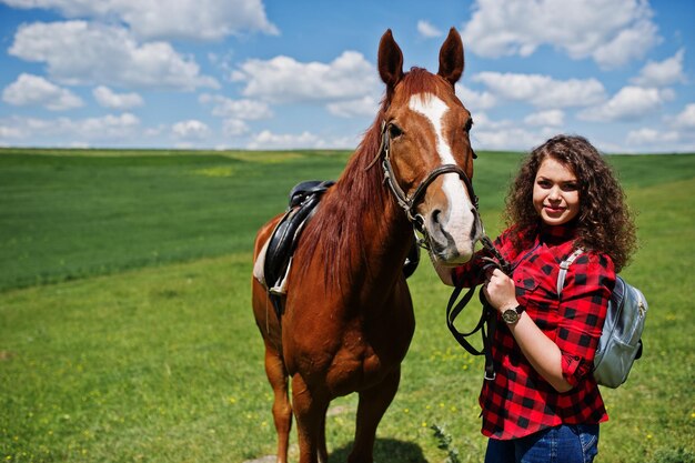 Una chica joven y bonita se queda con un caballo en un campo en un día soleado