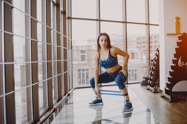 chica joven y bonita en un traje azul se dedica a deportes en el gimnasio