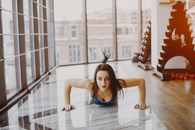 chica joven y bonita en un traje azul se dedica a deportes en el gimnasio