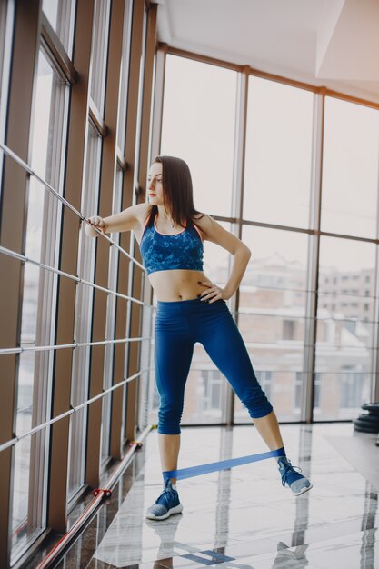 chica joven y bonita en un traje azul se dedica a deportes en el gimnasio