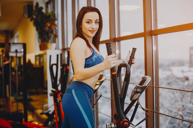 chica joven y bonita en un traje azul se dedica a deportes en el gimnasio