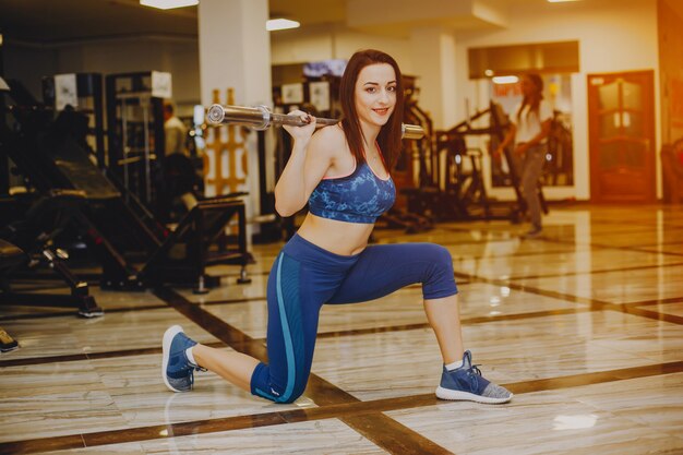 chica joven y bonita en un traje azul se dedica a deportes en el gimnasio