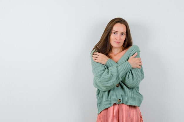 Chica joven con los brazos cruzados sobre el pecho en prendas de punto, falda y aspecto encantador. vista frontal.