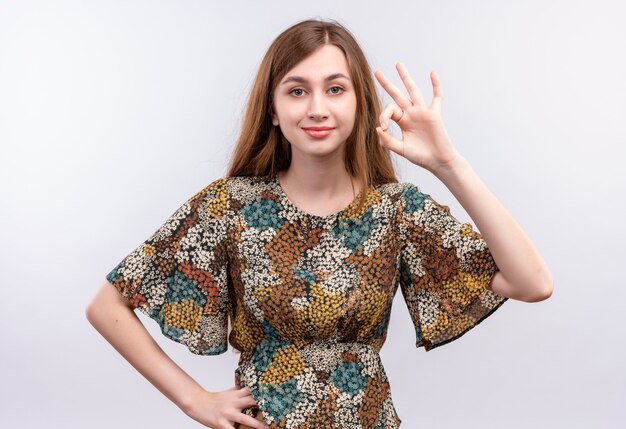 Chica joven con cabello largo vistiendo coloridos vestidos buscando confianza sonriendo haciendo bien firmar