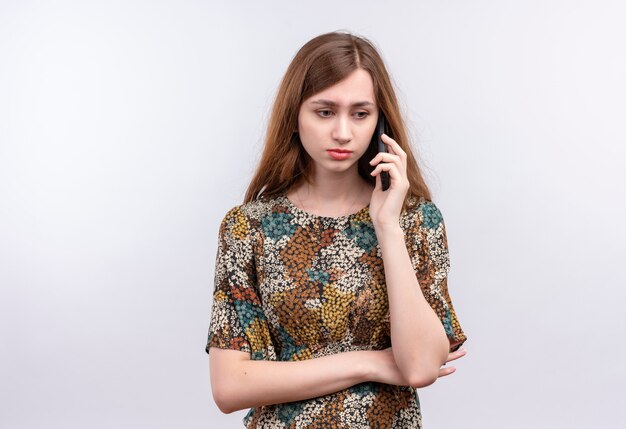 Chica joven con cabello largo vistiendo coloridos vestidos frunciendo el ceño mientras habla por teléfono móvil