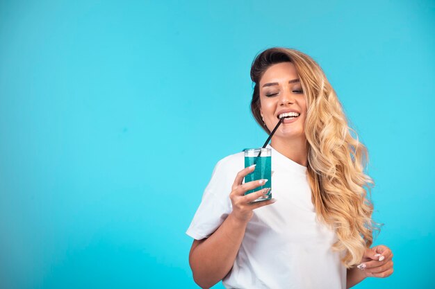 Chica joven en camisa blanca bebiendo cóctel azul.