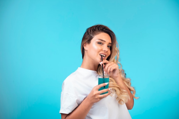 Foto gratuita chica joven en camisa blanca bebiendo cóctel azul
