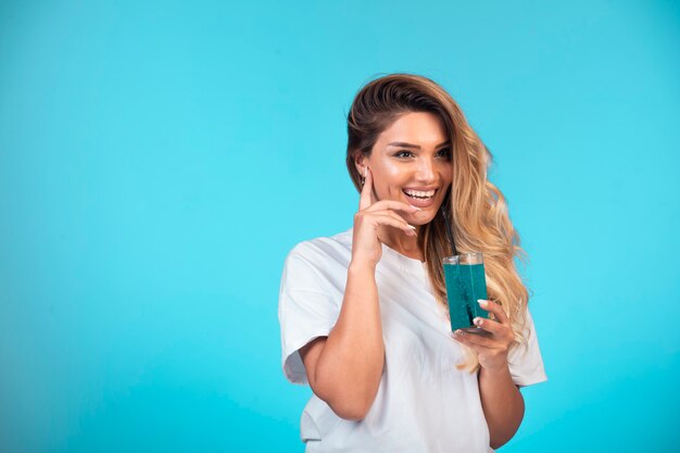 Chica joven con camisa blanca comprobando el sabor de la bebida azul y se siente feliz.