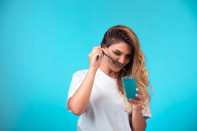 Chica joven con camisa blanca comprobando el sabor de la bebida azul.