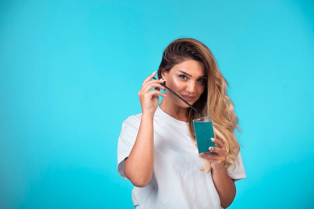 Chica joven con camisa blanca comprobando el sabor de la bebida azul.