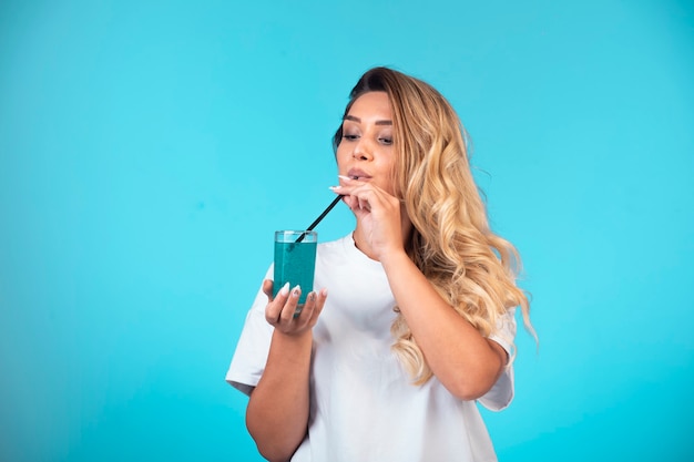 Chica joven con camisa blanca comprobando el sabor de la bebida azul.