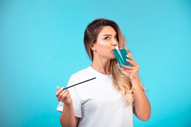 Chica joven con camisa blanca comprobando el sabor de la bebida azul.