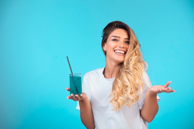Chica joven con camisa blanca sosteniendo una copa de cóctel azul y se siente positiva.