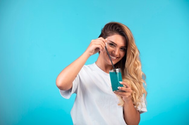 Chica joven con camisa blanca sosteniendo una copa de cóctel azul y se siente positiva.