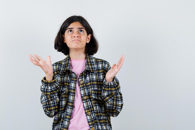 Chica joven en camisa a cuadros y camiseta rosa estirando las manos como sosteniendo algo pesado y mirando enfocado