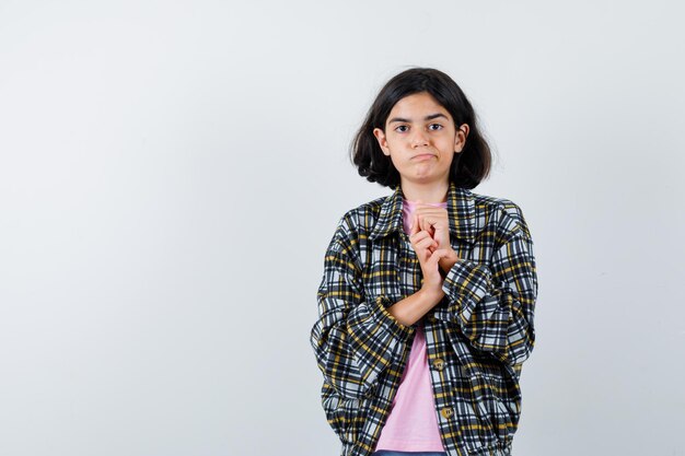 Chica joven en camisa a cuadros y camiseta rosa estrechando las manos y mirando bonita vista frontal.