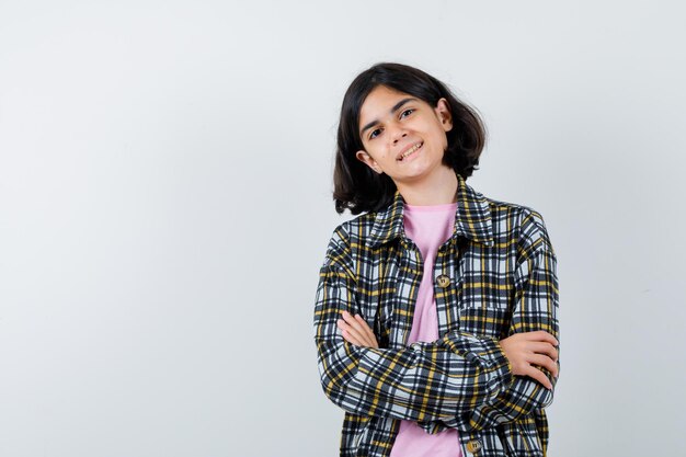 Foto gratuita chica joven en camisa a cuadros y camiseta rosa de pie con los brazos cruzados y mirando feliz, vista frontal.