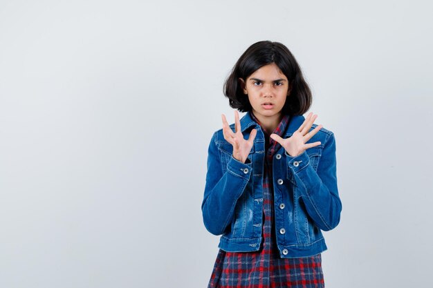 Chica joven en camisa de cuadros y chaqueta de jean estirando las manos como sosteniendo algo y mirando asustado, vista frontal.