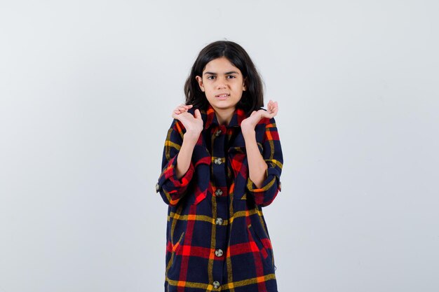 Chica joven en camisa de cuadros estirando las manos como sosteniendo algo y mirando amenazado, vista frontal.