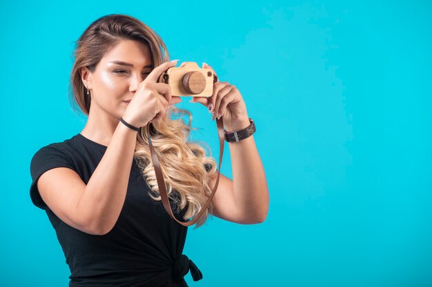 Chica joven en camisa negra colgó una cámara de juguete de su cuello y tomó una foto.