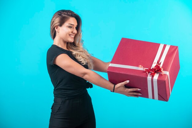 Chica joven en camisa negra sosteniendo una caja de regalo grande y se siente positiva.