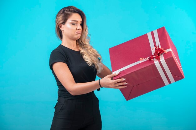 Chica joven con camisa negra sosteniendo una gran caja de regalo.