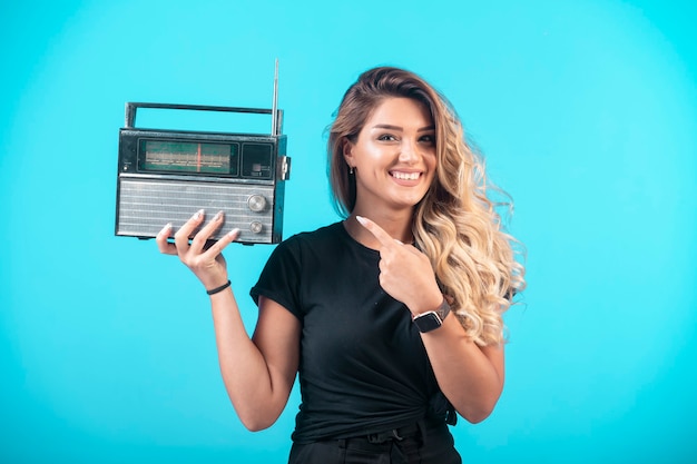 Foto gratuita chica joven con camisa negra sosteniendo una radio vintage y apuntando a ella.