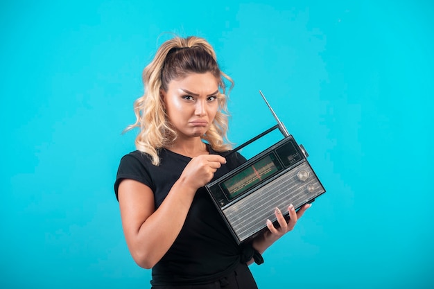 Chica joven en camisa negra sosteniendo una radio vintage y se siente decepcionada.