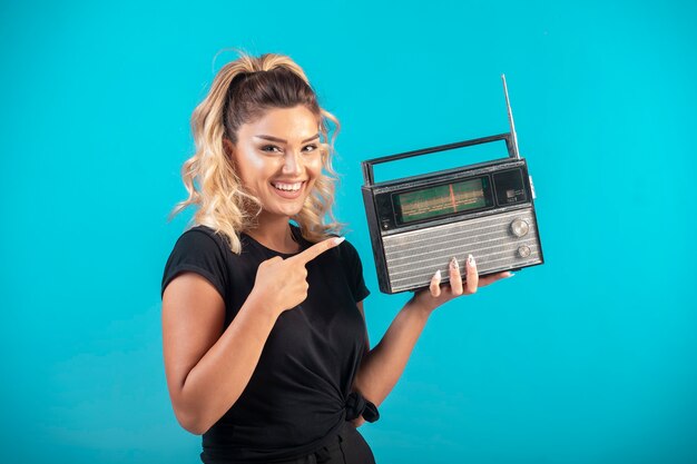 Chica joven con camisa negra sosteniendo una radio vintage y se siente positiva.