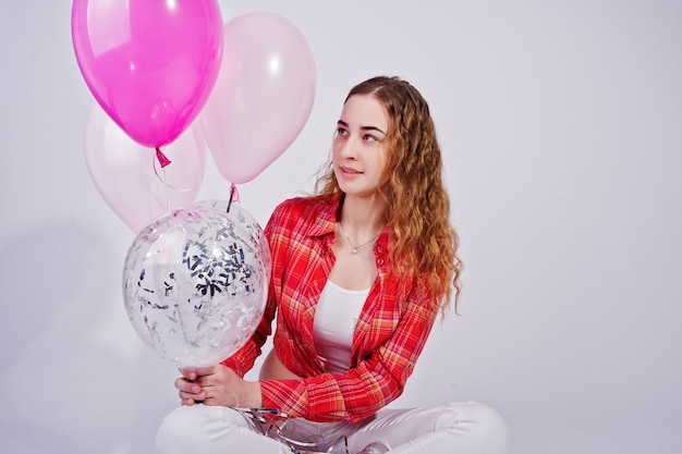 Chica joven en camisa roja a cuadros y pantalones blancos con globos contra fondo blanco en estudio