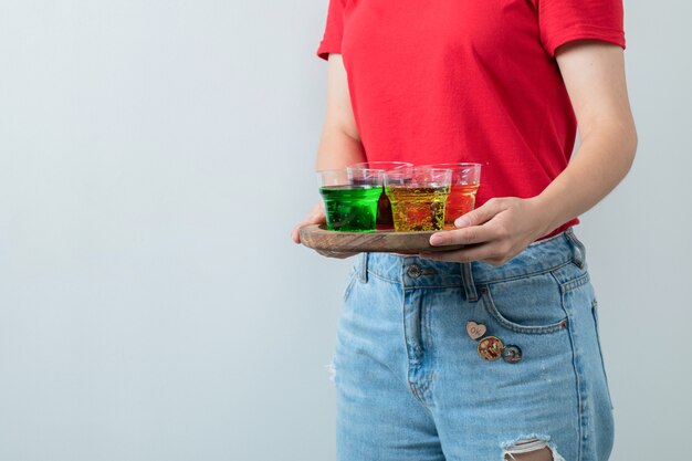 Chica joven en camisa roja sosteniendo una bandeja de madera de bebidas coloridas