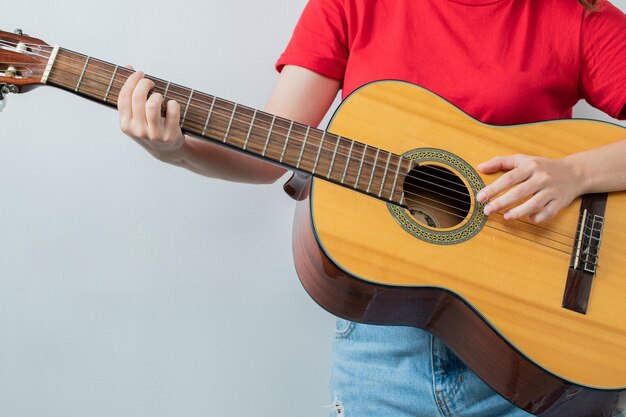 Chica joven en camisa roja sosteniendo una guitarra acústica