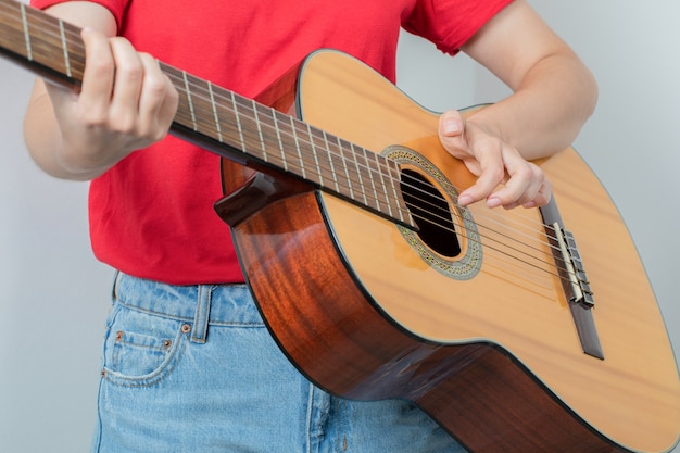 Chica joven en camisa roja sosteniendo una guitarra de madera