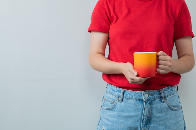 Chica joven en camisa roja sosteniendo una taza de bebida amarilla