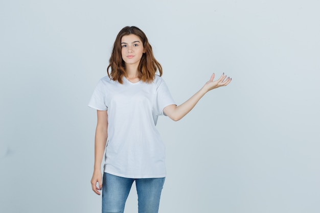 Chica joven en camiseta blanca fingiendo sostener algo y mirando confiada, vista frontal.