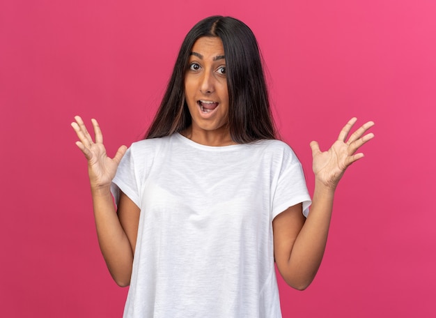 Chica joven en camiseta blanca gritando con los brazos levantados feliz y emocionado