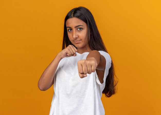 Chica joven en camiseta blanca mirando a la cámara con los puños cerrados posando como un boxeador mirando con cara seria