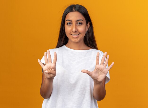 Chica joven en camiseta blanca mirando a la cámara sonriendo seguro mostrando el número ocho