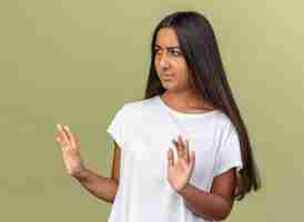 Foto gratuita chica joven en camiseta blanca mirando a un lado con cara seria haciendo gesto de parada
