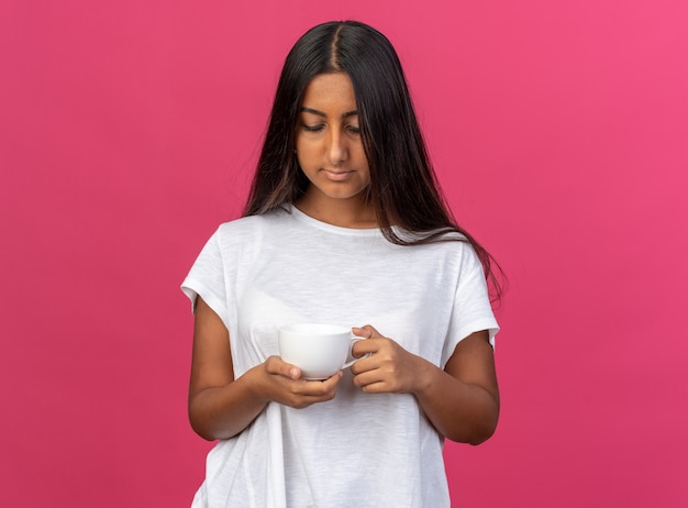 Chica joven en camiseta blanca sosteniendo una taza de café mirándolo con cara seria