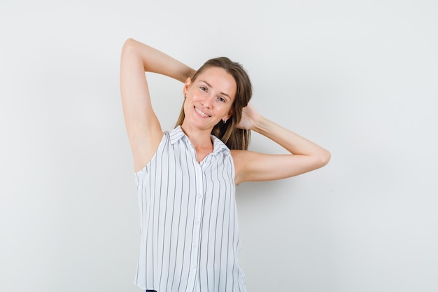 Chica joven en camiseta cogidos de la mano detrás de la cabeza y mirando atractiva, vista frontal.