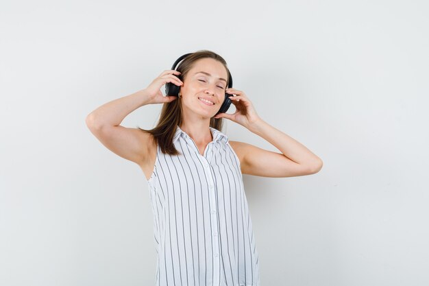 Chica joven en camiseta escuchando música con auriculares y mirando encantada, vista frontal.