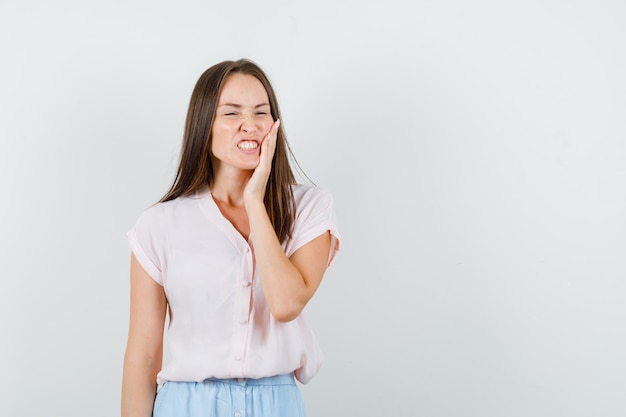 Chica joven en camiseta, falda que sufre de dolor de muelas y luce inquieta, vista frontal.