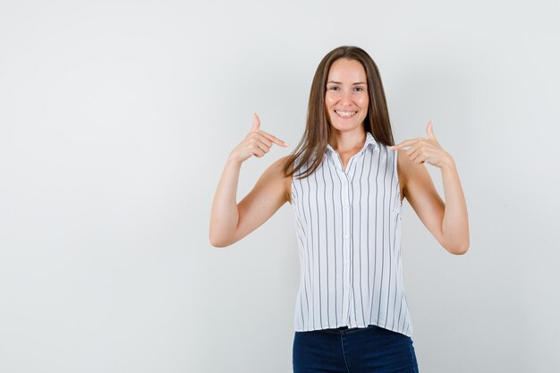 Foto gratuita chica joven en camiseta, jeans apuntando a sí misma y mirando alegre, vista frontal.