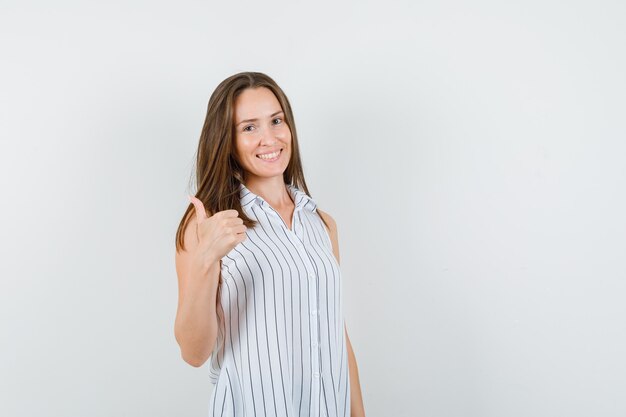 Chica joven en camiseta mostrando el pulgar hacia arriba y mirando alegre, vista frontal.