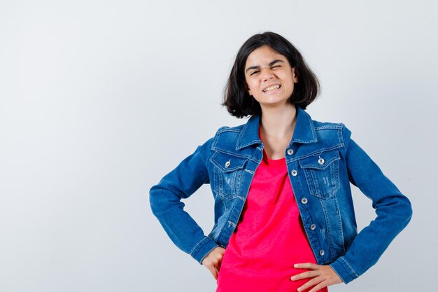 Foto gratuita chica joven en camiseta roja y chaqueta de jean cogidos de la mano en la cintura y mirando feliz