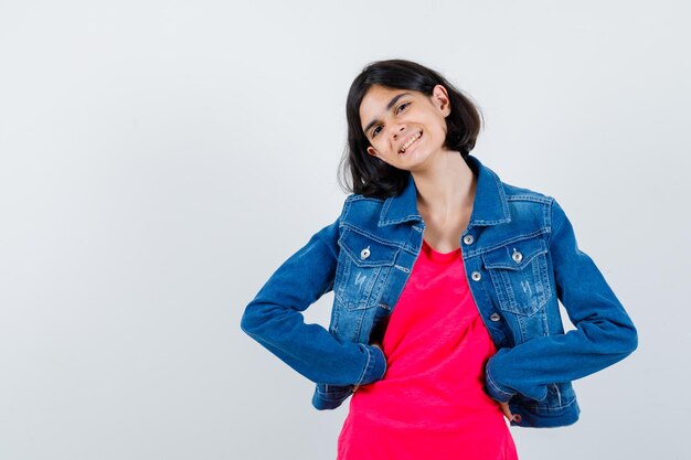 Chica joven en camiseta roja y chaqueta de jean cogidos de la mano en la cintura, sonriendo y mirando feliz